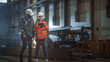 © Gorodenkoff - Two Heavy Industry Engineers Walk in Steel Factory, Use Tablet and Discuss Work. Industrial Worker Uses Angle Grinder in the Background. Black African American Specialist Talks to Female Technician.