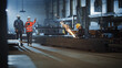 © Gorodenkoff - Two Heavy Industry Engineers Walk in Steel Factory, Use Tablet and Discuss Work. Industrial Worker Uses Angle Grinder in the Background. Black African American Specialist Talks to Female Technician.