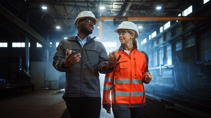 Aufkleber - Two Heavy Industry Engineers in Hard Hats Walk in Steel Metal Manufacturing Factory and Have a Discussion. Black African American Industrial Specialist Talk to Female Technician in Manufacture.