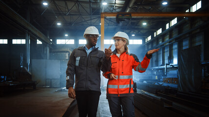 Aufkleber - Two Heavy Industry Engineers in Hard Hats Walk in Steel Metal Manufacturing Factory and Have a Discussion. Black African American Industrial Specialist Talk to Female Technician in Manufacture.