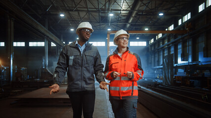 Aufkleber - Two Heavy Industry Engineers in Hard Hats Walk in Steel Metal Manufacturing Factory and Have a Discussion. Black African American Industrial Specialist Talk to Female Technician in Manufacture.