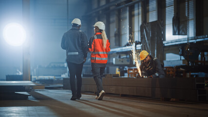 Aufkleber - Two Heavy Industry Engineers Walk in Steel Factory, Use Tablet and Discuss Work. Industrial Worker Uses Angle Grinder in the Background. Black African American Specialist Talks to Female Technician.