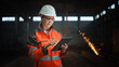 © Gorodenkoff - Professional Heavy Industry Engineer/Worker Wearing Safety Uniform and Hard Hat Uses Tablet Computer. Serious Successful Female Industrial Specialist Standing in a Metal Manufacture Warehouse.