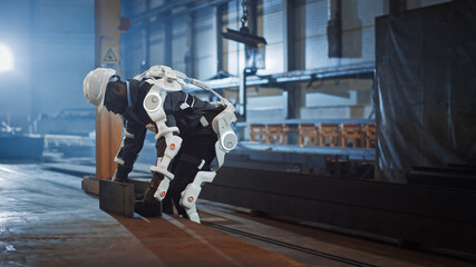 Poster - Black African American Engineer is Testing a Futuristic Bionic Exoskeleton and Picking Up Metal Objects in a Heavy Steel Industry Factory. Contractor is Heavy Lifting Steel Parts in a Powered Shell.