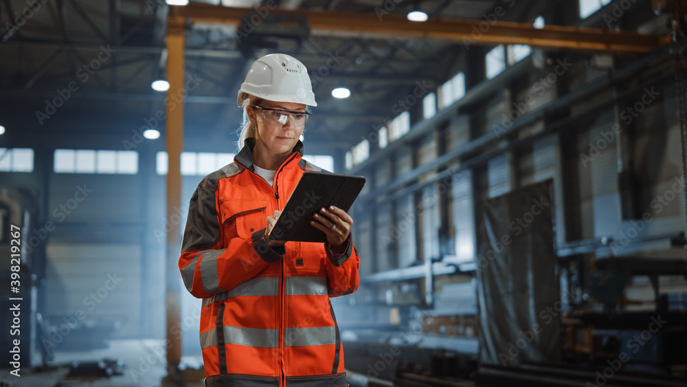 Professional Heavy Industry Engineer Worker Wearing Safety Uniform and Hard Hat, Using Tablet Computer. Serious Successful Female Industrial Specialist Walking in a Metal Manufacture Warehouse. - obrazy, fototapety, plakaty 
