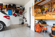 Home Suburban Car Garage Interior With Wooden Shelf, Tools Equipment Stuff Storage Warehouse On White Wall Indoor. Vehicle Parked At House Parking Background. DIY Workbench For Repair Home Appliances