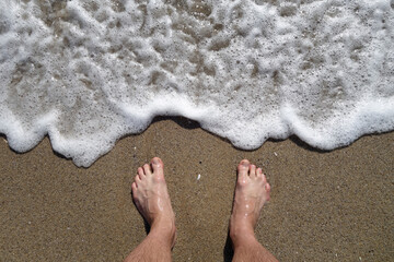 Man's feet from top and sea wave and sand.