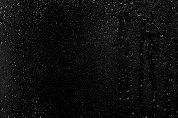 Drops of water flow down the surface of the clear glass on a black background. Texture for creativity.