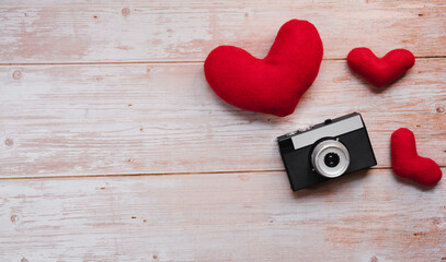 Wooden flat lay background for Valentines day holiday on February 14. Three red stuffed plush toy hearts and black with silver old retro film camera.