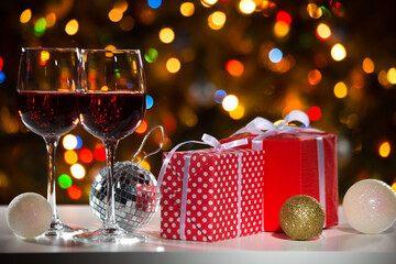 Canvas Print - Glasses of wine and Christmas gifts and balls on the background of Christmas lights