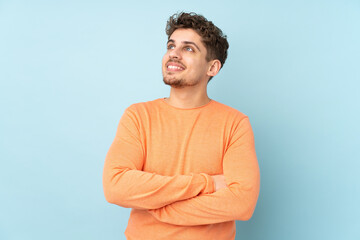 Wall Mural - Caucasian man isolated on blue background looking up while smiling