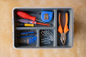 toolbox. red and yellow screwdriver, electronics repair tool kit, electrical tester screwdriver, orange pliers, screw, blue tape measure. yellow wooden workshop bench. home hobby in lockdown. 