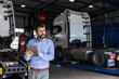 © Dusan Petkovic - Young serious bearded CEO standing in garage of shipping firm and using tablet. In background are trucks.