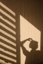 Silhouette Of Young Woman Thinking With Her Hand Touching Her Head In The Morning At Home. Contrast Window Shadows On The Wall. Aesthetic Shade Portrait. Lights And Shades. Shade Silhouette.