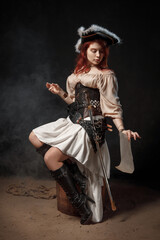 Young pirate female with long red hair. Woman is wearing a black corset bustier, tricorn hat , gun belt and armed with a pistol and sword.