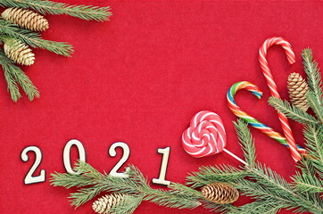 Wall Mural - Congratulatory background for cards and congratulations with place for text.Fir branches, numbers 2021 and caramel candies on a red felt background lying on a wooden table.