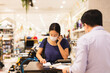 © bignai - Woman in protective mask talking on cell phone cashier counter.