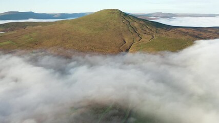 Wall Mural - Aerial view flying over a layer of fog and cloud towards a mountain