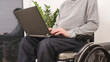 © 24K-Production - Young man in wheelchair with laptop working remotely from home, using internet and looking at screen.