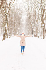 Young girl in a snowy forest in winter. Portrait of a girl in a winter park with running snow. A woman goes catching snowflakes