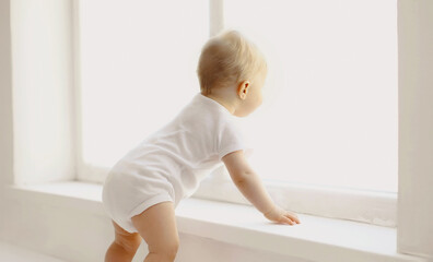 little baby looking out the window in white room at home