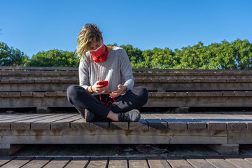 Sticker - Shot of a sitting woman in a protective mask with headphones talking by phone - new normal