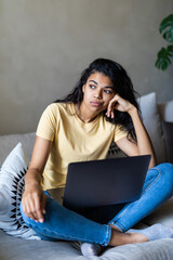 Young attractive and bored latin woman working at home living room sitting on couch with laptop computer in stress looking sad and tired in freelance entrepreneur lifestyle concept