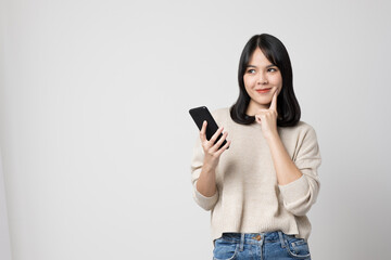 Smiling young asian woman holding smartphone standing on isolated white background.