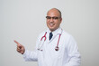 © Chanakon - Doctor in white coat, stethoscope pointing finger to beside look into camera.with smile isolated on white background.