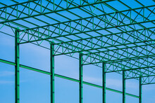 Low Angle View Of Green Steel Roof Of Warehouse Building Structure In Construction Area Against Blue Sky Background