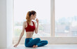 © SHOTPRIME STUDIO - Side view of a woman in blue leggings sitting on a windowsill and a red t-shirt yoga fitness