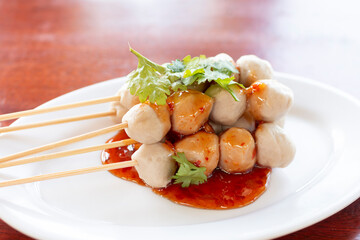 Close up Grilled pork balls with sweet spicy sauce on wooden table. Pork ball stick by bamboo skewers with homemade sauce. Grilled Pork ball topping by spicy and sweet sauce plate on table.