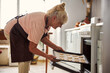 © Svitlana - Joyful senior woman putting tray with cookies into oven