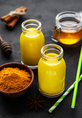 Wall Mural - Yellow turmeric latte drink. Golden milk with cinnamon, turmeric, ginger  and honey over black concrete background.