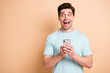 © deagreez - Portrait of nice cheerful amazed guy blogger using gadget looking aside copy space advert isolated over beige pastel color background