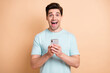 © deagreez - Portrait of nice cheerful amazed addicted guy blogger using gadget having fun isolated over beige pastel color background