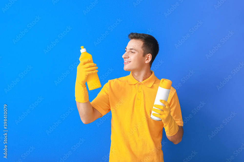 Young man with cleaning supplies on color background