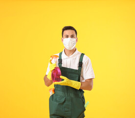 Poster - Young male janitor in medical mask and with cleaning supplies on color background