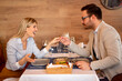 Beautiful young couple is looking at each other and smiling during their date in a restaurant, man is holding his girlfriend's hand