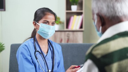 Wall Mural - Shoulder shot, young doctor or nurse writing prescription during home visiting to sick senior man while both worn face mask due to coronavirus covid-19 pandemic as safety measures