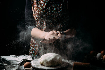 Making dough by hands at bakery or at home. Flour cloud in the air. Close up of woman chef hands preparing for kneading the dough on the table, powdering with flour