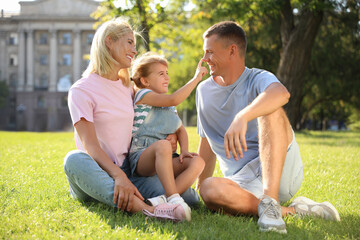 Poster - Happy parents with their child having fun on green grass. Spending time in nature