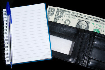 notebook with a blue pen on , next to a black leather wallet with US dollar bills. selective focus