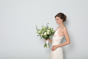 Wall Mural - Young bride wearing wedding dress with beautiful bouquet on light grey background. Space for text