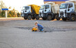 © Anna - cute toddler boy interestedly plays with toy dump truck on control panel sitting on asphalt. behind him are 3 large real dump trucks. sunny warm day. Favorite games for boys, happy childhood