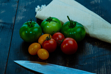 Canvas Print - High angle shot of ripe and unripe tomatoes with knife and napkin on a wooden table