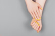 Woman hands with yellow manicure on the gray background.