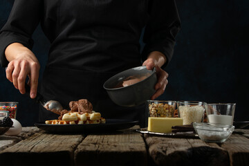 Close-up view of chef pours ice-cream ball for serving waffles on rustic wooden table with ingredients on dark blue background. Backstage of cooking sweet dessert for breakfast. Frozen motion.