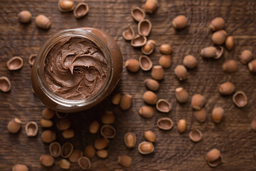 Chocolate-nut paste spread in a glass jar on a wooden background top view