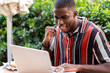 © Ezequiel Gimenez/Westend61 - Happy young man clenching fist while using laptop on terrace of cafe